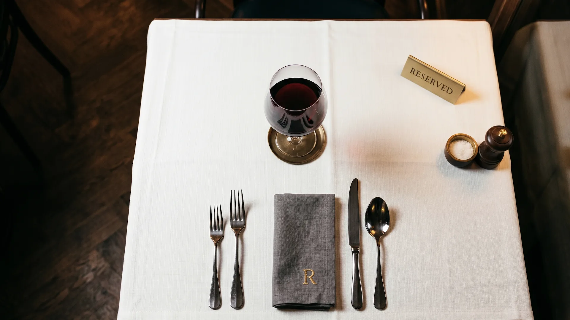 Vista cenital de una mesa de restaurante elegante reservada y vacía con mantel blanco, cubiertos dispuestos y copa de vino, simbolizando el coste de un no-show en hostelería